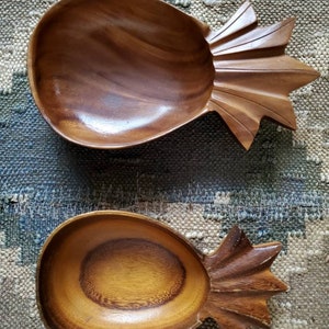Puede incluir: Dos cuencos de madera con forma de piña. Los cuencos están hechos de madera marrón oscura y tienen un diseño de piña tallado. Los cuencos son perfectos para servir aperitivos o fruta.