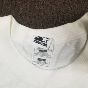 May include: White t-shirt with a black Starter logo and a white star. The tag says "XL" and "100% Cotton".
