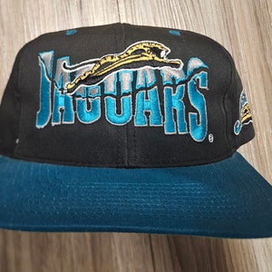 May include: Black and teal baseball cap with the Jacksonville Jaguars logo. The logo features a teal jaguar with a gold outline and the word "Jaguars" in teal with a silver outline.