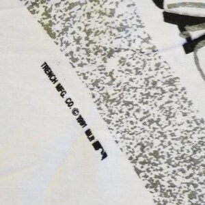 Puede incluir: Una camiseta blanca con un estampado gr&aacute;fico en blanco y negro. El texto "TRENCH MFG. CO. &copy; 1991 MLB" est&aacute; impreso en la parte inferior de la camiseta.