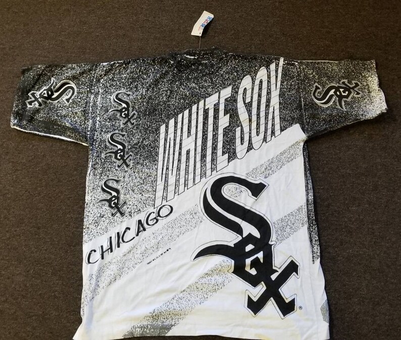Puede incluir: Camiseta blanca con un estampado en blanco y negro del logotipo de los Chicago White Sox y las palabras "White Sox" y "Chicago".