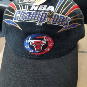 May include: Black baseball cap with a gold embroidered NBA Champions logo and a red, white, and blue patch with a bull's head and the years 91, 92, 93, 96, 97, and 98.