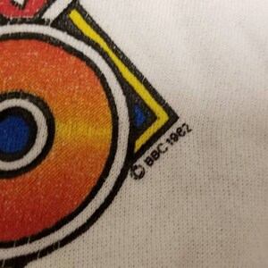 May include: A white t-shirt with a colorful geometric design and the copyright symbol and text "BBC 1982".