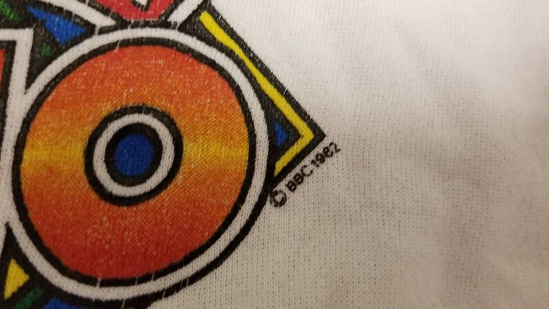 May include: A white t-shirt with a colorful geometric design and the copyright symbol and text "BBC 1982".