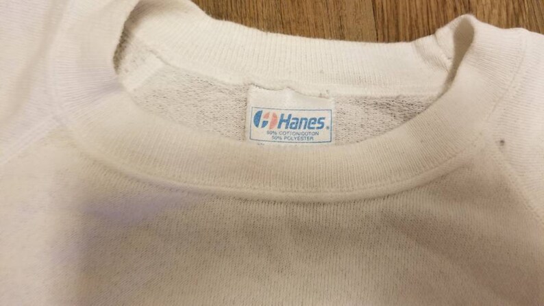 May include: White Hanes sweatshirt with a blue tag that reads "Hanes" and "60% Cotton/40% Polyester".