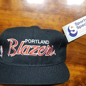 May include: Black Portland Blazers baseball cap with the team name in red and white embroidery. The cap has a flat brim and a tag from Sports Specialties.
