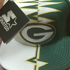 May include: Green Bay Packers Starter hat with a white and green lightning bolt design. The hat has a green and white "G" logo on the front and a Starter tag on the side. The hat is new with tags.