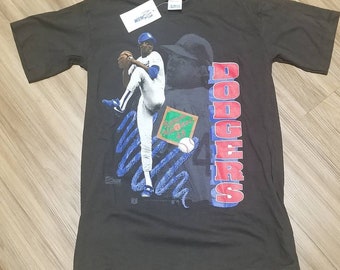 Puede incluir: Camiseta negra con un gráfico de un jugador de béisbol lanzando, una pelota de béisbol y la palabra "DODGERS" en letras rojas y azules.