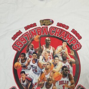 May include: White t-shirt with a red, black, and white graphic of the Chicago Bulls NBA Champions from 1991, 1992, 1993, and 1996. The graphic features a red bull mascot and a group of basketball players, including Michael Jordan.