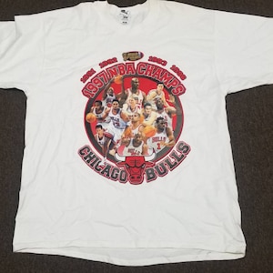 May include: White t-shirt with a graphic of the Chicago Bulls basketball team. The graphic features the team's logo and the text "1991 1992 1993 1996 1997 NBA CHAMPS Chicago Bulls".