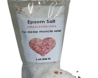 May include: A clear plastic bag filled with white Epsom salt with pink Himalayan Shea salt. The bag has a label that reads "Epsom Salt Himalayan Shea for deep muscle relief 1 LB (448 G)".