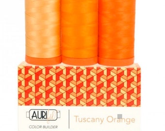May include: Three spools of orange thread sit atop a box with a geometric pattern. The thread colors range from light peach to bright orange. The box is labeled "Tuscany Orange" and "Color Builder".