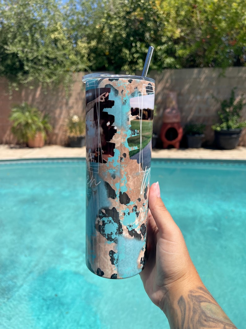 K&ouml;nnte beinhalten: Ein Edelstahlbecher mit Deckel und Strohhalm. Der Becher hat ein t&uuml;rkisfarbenes, braunes und schwarzes Kuhfellmuster mit wei&szlig;er Schrift. Der Becher wird von einer Person in der N&auml;he eines Swimmingpools gehalten.