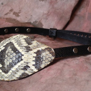 May include: A black leather eye patch with a snakeskin design. The patch has a strap with silver studs.