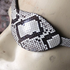 May include: A black and white snakeskin eye patch with a strap. The patch is made of real snakeskin and has a unique pattern.