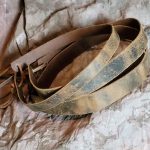 May include: Three brown leather straps with a distressed look. The straps are folded and stacked on top of each other.