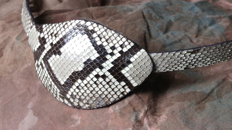 May include: A black and white snakeskin eye patch with a strap. The eye patch is made of real snakeskin and has a unique pattern.