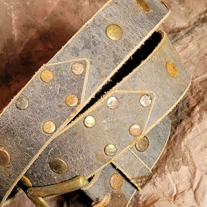 May include: A brown leather belt with brass studs. The belt is folded in half and the buckle is visible.