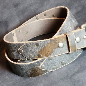 May include: A gray leather belt with silver studs and a silver buckle. The belt is worn and has a distressed look.
