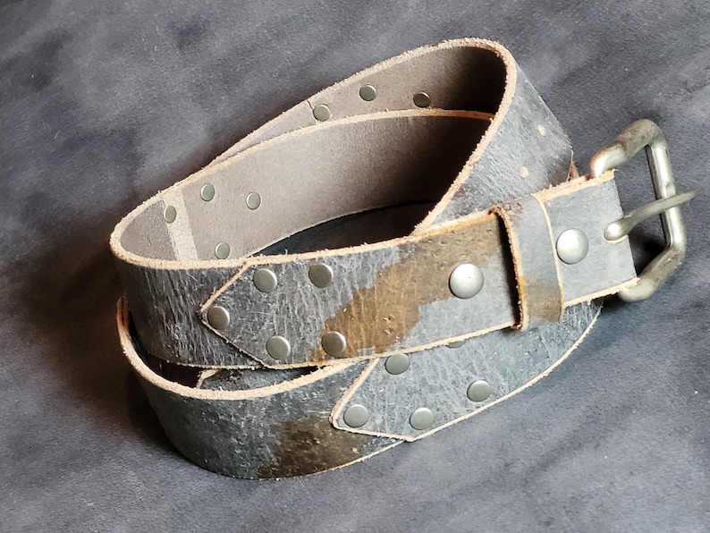 May include: A gray leather belt with silver studs and a silver buckle. The belt is worn and has a distressed look.