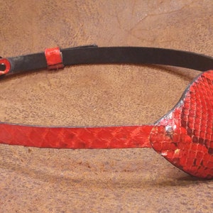 May include: A red leather eye patch with a snakeskin pattern. The patch is attached to a black leather strap with a buckle.