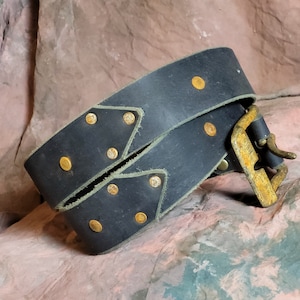 May include: A black leather belt with a brass buckle and gold-toned rivets. The belt is folded in half and the buckle is visible.