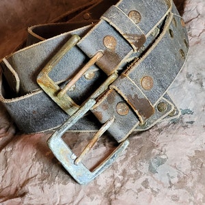May include: A worn leather belt with a silver buckle and multiple rows of rivets. The belt is folded and the buckle is in focus.