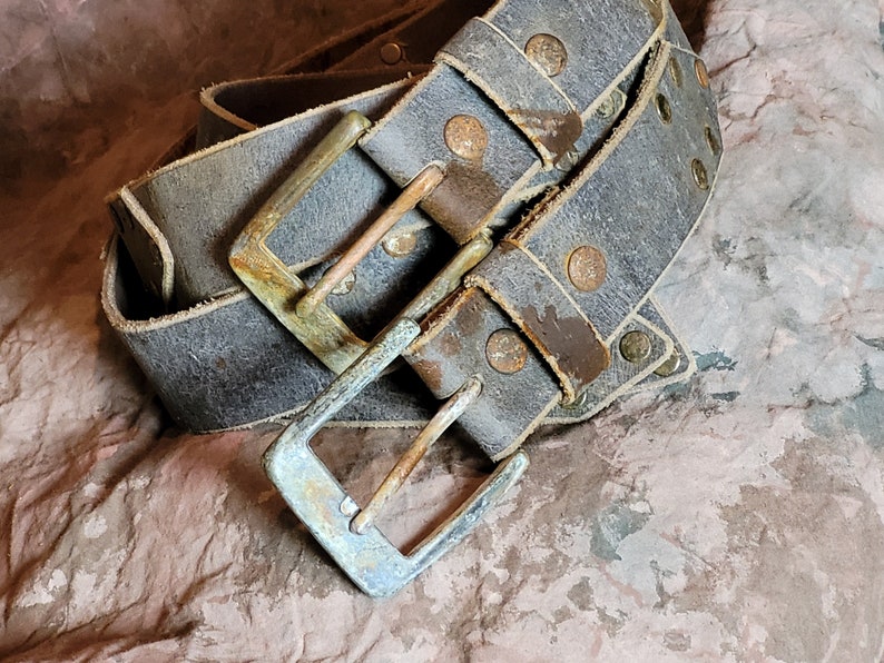 May include: A worn leather belt with a silver buckle and multiple rows of rivets. The belt is folded and the buckle is in focus.