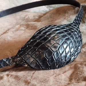 May include: A black leather eye patch with a snakeskin pattern. The patch is attached to a black leather strap.