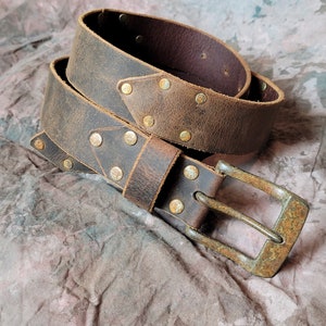 May include: A brown leather belt with a distressed finish and brass rivets. The belt has a silver buckle.
