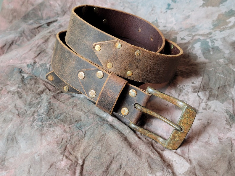 May include: A brown leather belt with a distressed finish and brass rivets. The belt has a silver buckle.