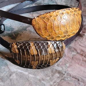 May include: Two brown leather eye patches with a snakeskin pattern. The eye patches are made of real snakeskin and have a light brown and dark brown color.
