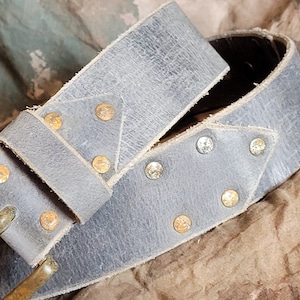 May include: A gray leather belt with a brass buckle and decorative metal studs. The belt is folded in half and the buckle is visible.