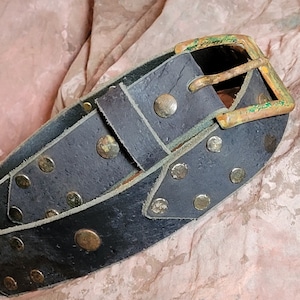 May include: A black leather belt with brass studs and a brass buckle. The buckle has a green patina.