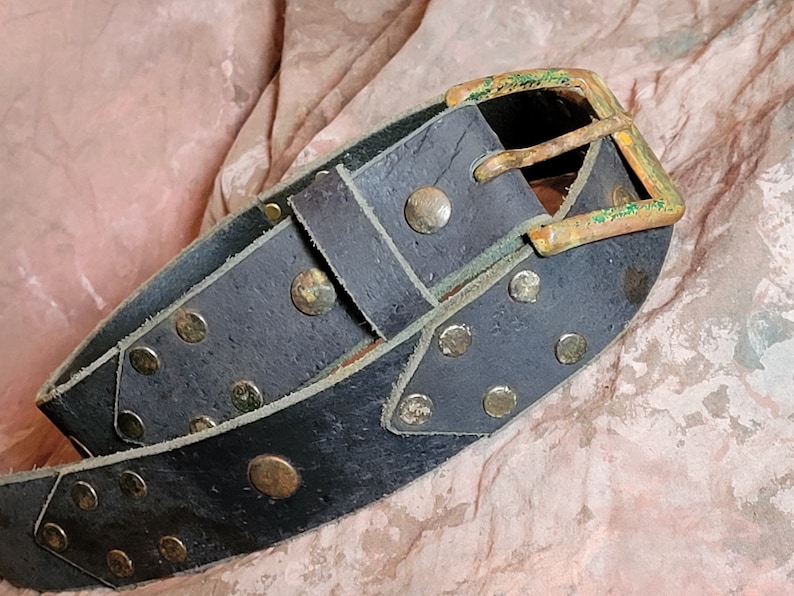 May include: A black leather belt with brass studs and a brass buckle. The buckle has a green patina.