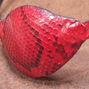 May include: A red leather eye patch with a snakeskin pattern. The patch is made of genuine leather and has a black strap.