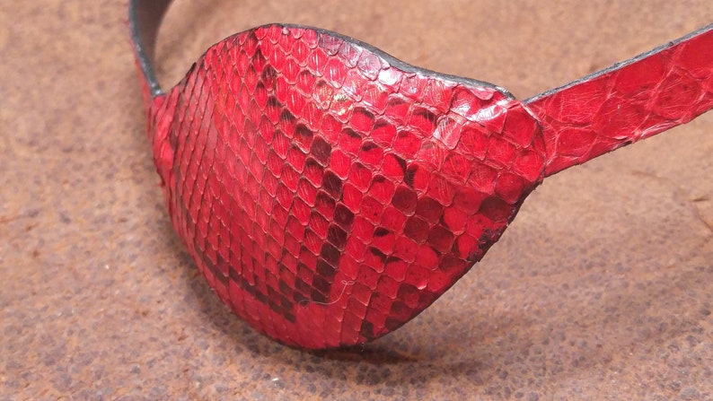 May include: A red leather eye patch with a snakeskin pattern. The patch is made of genuine leather and has a black strap.