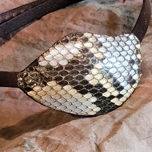 May include: A brown leather eye patch with a snakeskin pattern. The patch is made of genuine leather and has a unique design.