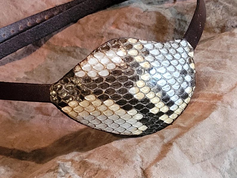 May include: A brown leather eye patch with a snakeskin pattern. The patch is made of genuine leather and has a unique design.