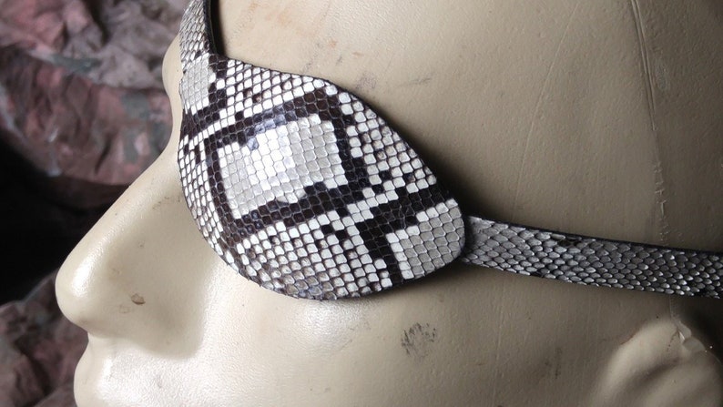 May include: A black and white snakeskin eye patch with a strap. The patch is made of real snakeskin and has a unique pattern.