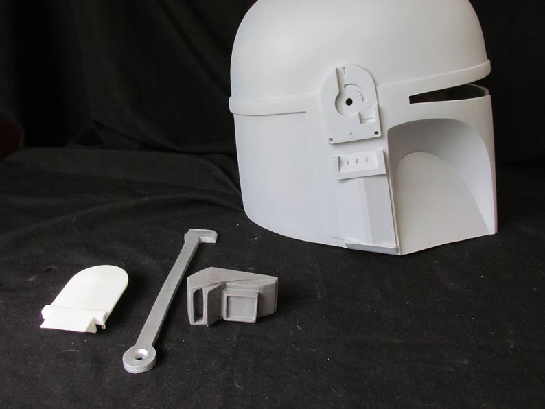 May include: A white Mandalorian helmet with separate components, including a visor, side pieces, and a connecting bar. The helmet has a smooth, matte finish and is designed for cosplay or display.