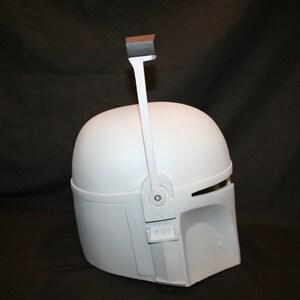 May include: A white Mandalorian helmet with a visor and a rangefinder. The helmet has a smooth, matte finish and is designed with angular shapes. The rangefinder is attached to the top of the helmet.