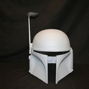 Op de afbeelding: Een matte witte helm met een gladde, ronde koepel, een T-vormige vizieropening en een verticale afstandsmeterstang aan de rechterkant. De helm heeft een schoon, onbeschilderd oppervlak zonder extra markeringen of decoratieve details.