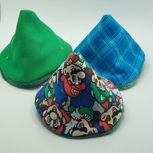 May include: Three fabric cone-shaped toys. One is green, one is blue with a white checkered pattern, and one is blue with a multi-colored Mario character print.