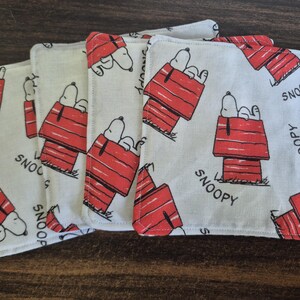 Pu&ograve; includere: Set di sottobicchieri quadrati in tessuto con un motivo ripetuto di Snoopy nella sua cuccia rossa. La parola "SNOOPY" &egrave; stampata sui sottobicchieri. I sottobicchieri sono bianchi con dettagli rossi e neri.