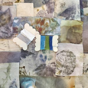 May include: A collection of fabric swatches in various shades of blue, green, brown, and white, with a few pieces of embroidery floss on wooden spools.