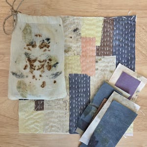 May include: A collection of handmade textile art pieces. Includes a small drawstring bag with botanical prints, a patchwork textile with visible stitching, and several rectangular fabric swatches in various colors and textures. The color palette is muted, with natural tones.