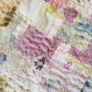 May include: A patchwork quilt made of various shades of pink, beige, and brown fabric. The quilt is stitched together with a running stitch, creating a rustic and handmade look.