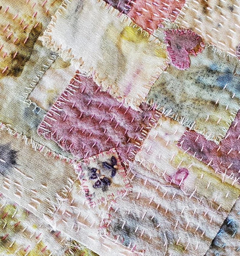 May include: A patchwork quilt made of various shades of pink, beige, and brown fabric. The quilt is stitched together with a running stitch, creating a rustic and handmade look.
