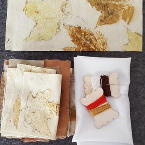 May include: A set of fabric squares with leaf patterns in shades of brown and beige, along with white fabric and spools of red, brown, and yellow thread.